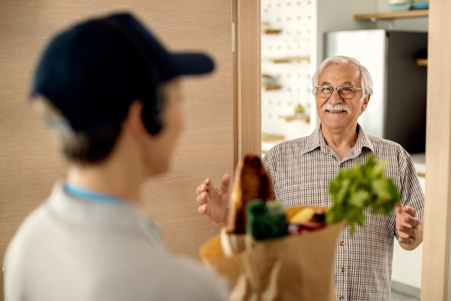 Happy mature man receiving groceries delivery at home.